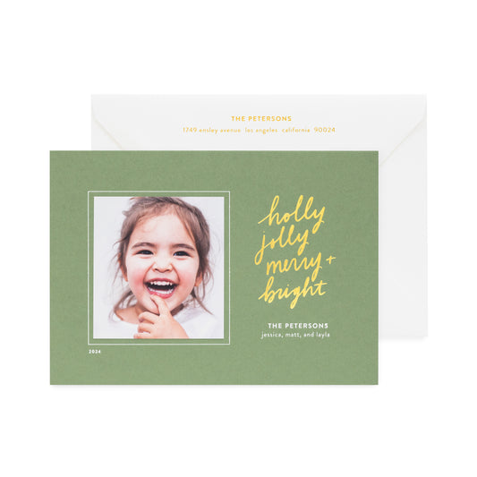 moss green holiday photo card printed with holly jolly merry bright in gold foil paired with a white envelope