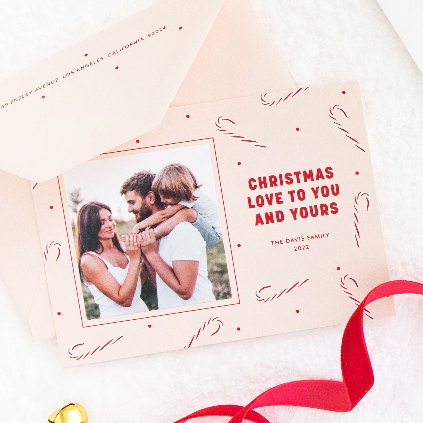 Pink custom holiday photo card printed with white and red candy cane pattern and 'christmas love to you and yours' with a photo of a family with a little boy