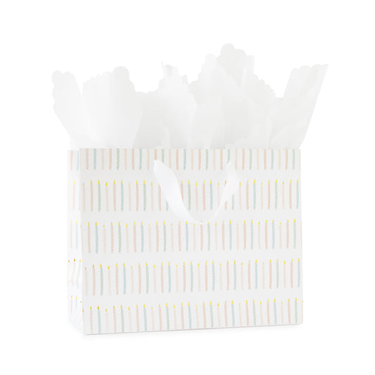 large gift bag with white ribbon handles printed with a colorful candle pattern in pink and blue with gold foil with white scallop tissue paper