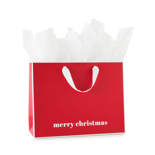 A red Christmas gift bag with white handles and the words 'merry christmas', printed in white at the bottom, with white piped edges, filled with white tissue paper