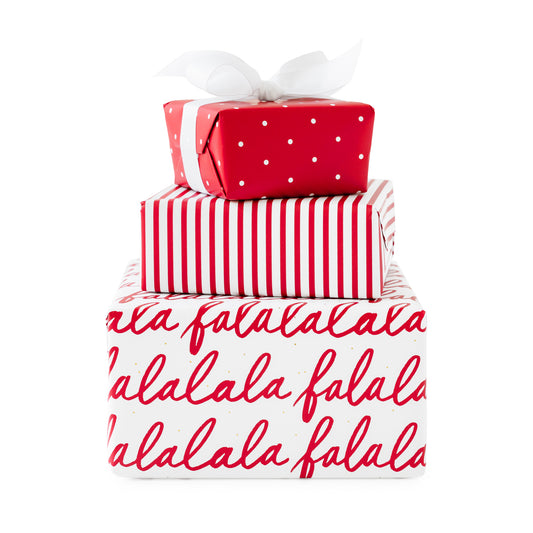 Stack of three wrapped gifts, bottom wrapped in white wrap with red falalala messaging, white with red stripes, and red with white swiss dot tied with a white bow on top