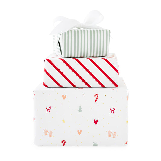 Three stacked gift boxes wrapped in festive holiday paper. The top box is wrapped in white and light green striped paper with a white ribbon bow, middle is a red and white stripe, and bottom box has a holiday icon pattern