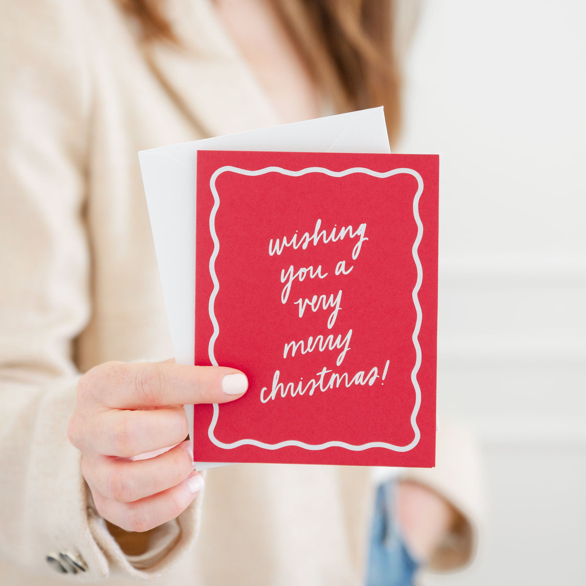 Person holding a red Christmas card with 'wishing you a very merry christmas' paired with a white envelope
