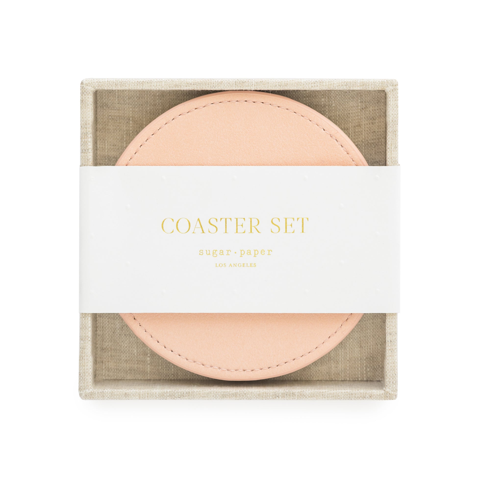 A set of pink vegan leather coasters with a fabric tray holder, packaged for sale with 'coaster set' and sugar paper logo printed on a white belly band in gold foil