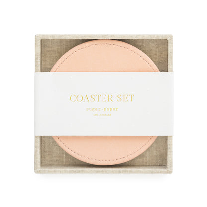 A set of pink vegan leather coasters with a fabric tray holder, packaged for sale with 'coaster set' and sugar paper logo printed on a white belly band in gold foil
