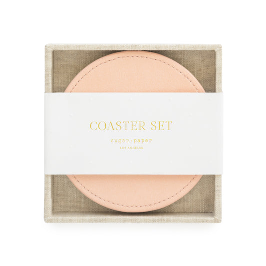 A set of pink vegan leather coasters with a fabric tray holder, packaged for sale with 'coaster set' and sugar paper logo printed on a white belly band in gold foil