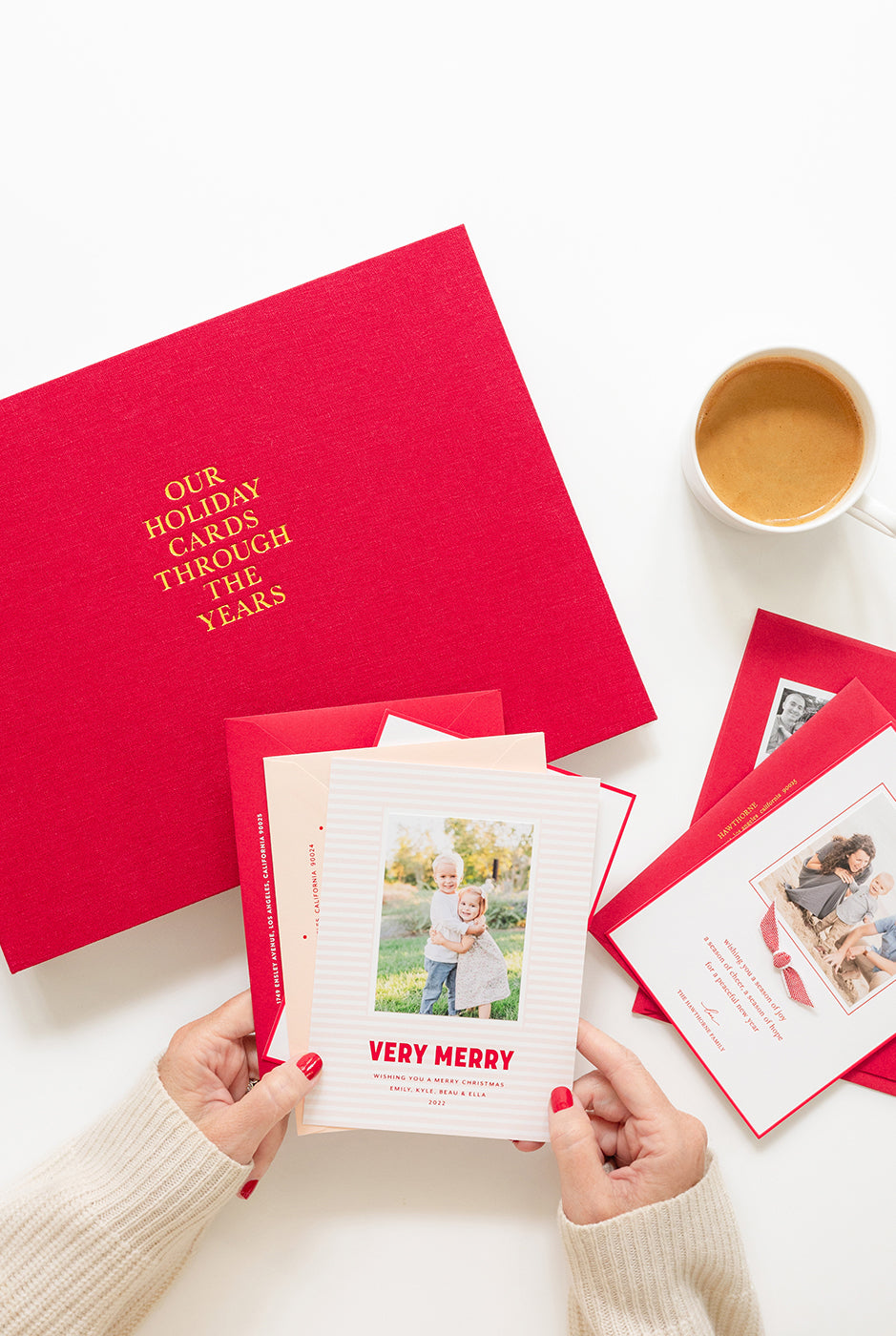 Red holiday card album with cards and a cup of coffee on a white surface