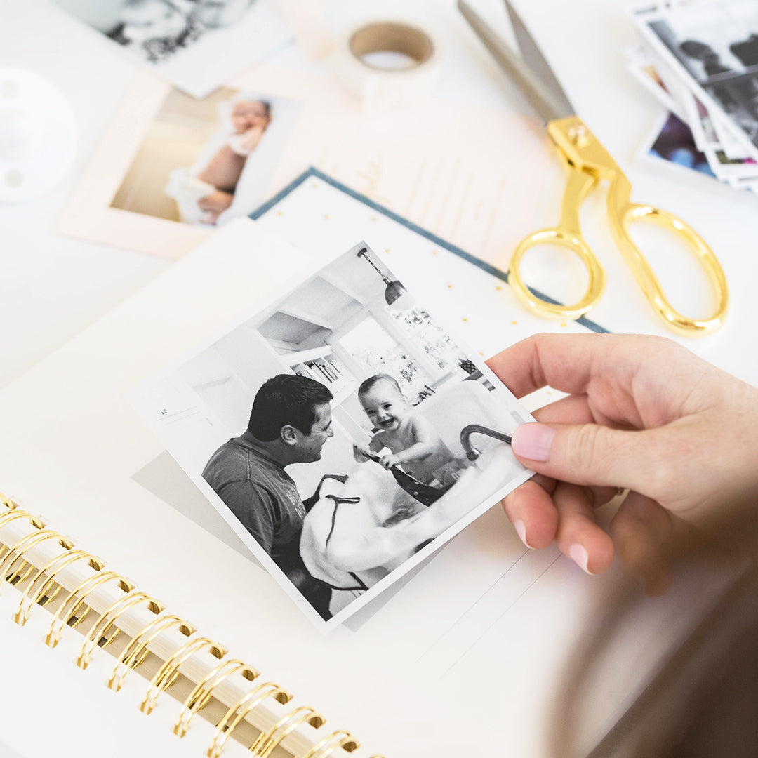 Hand placing a photo of baby in bath with dad next to her and other photos around into baby book