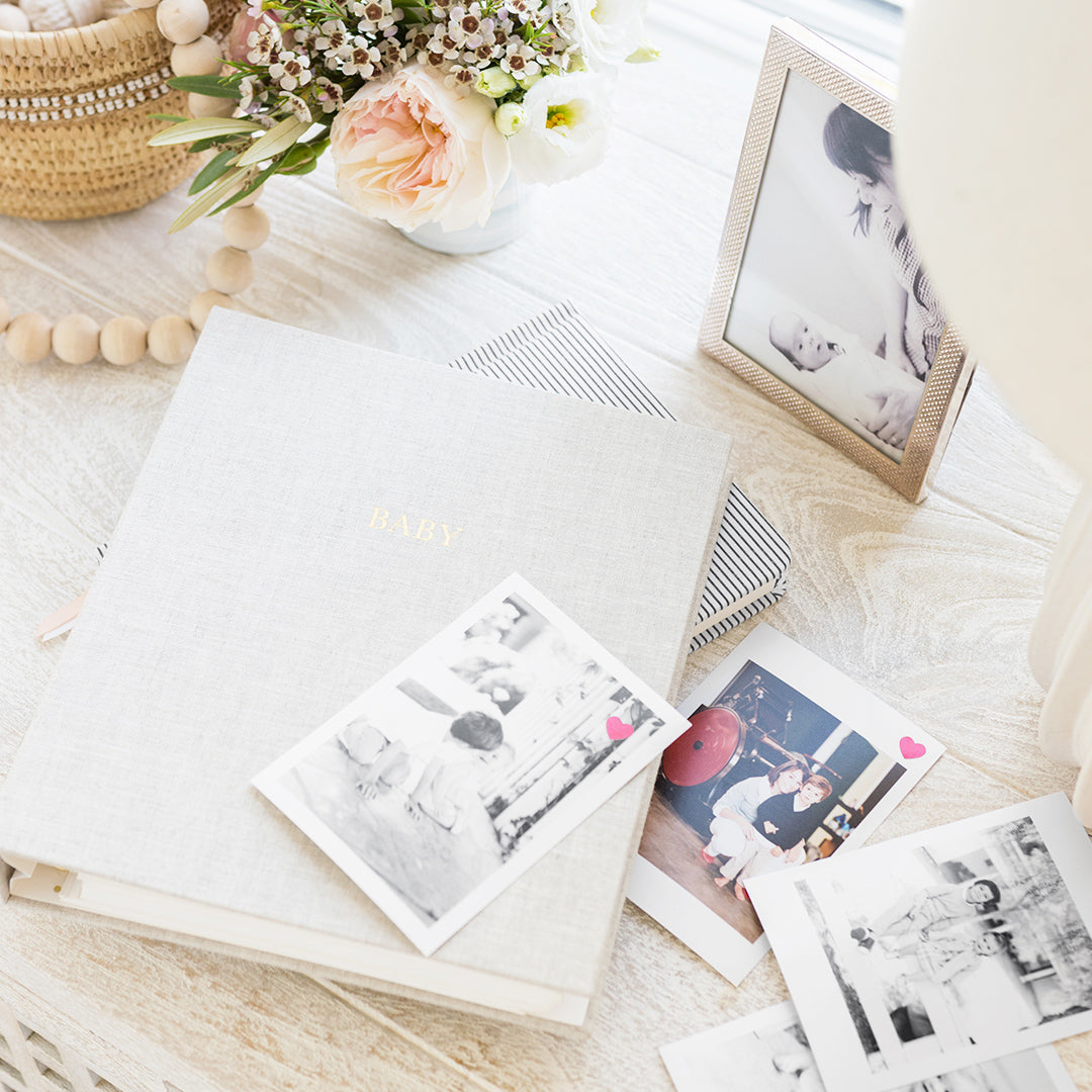 flax baby book with 'baby' on cover in gold foil on a table with baby and family photos