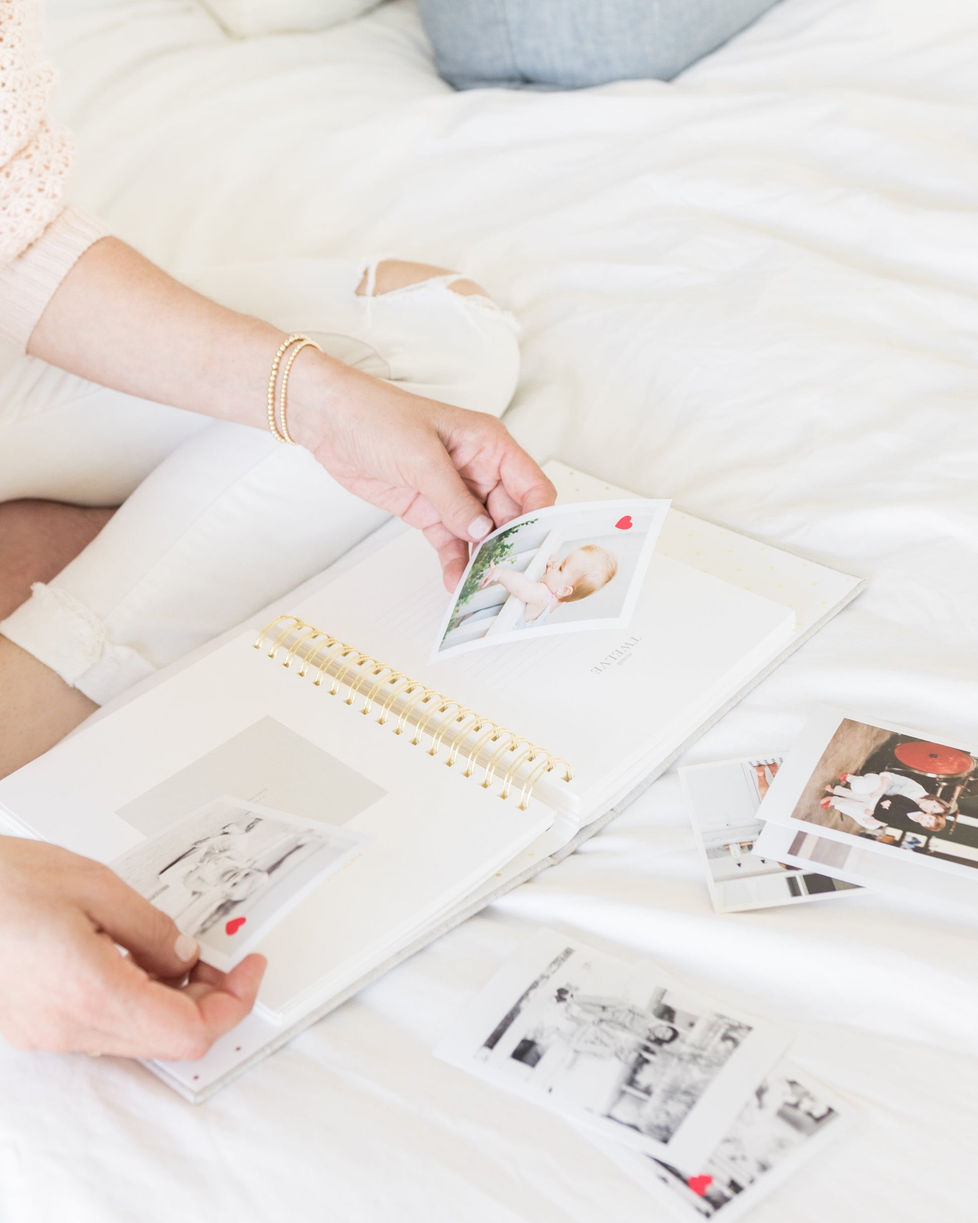 Inside of baby book with photos in hand and laid out on bed in front of person