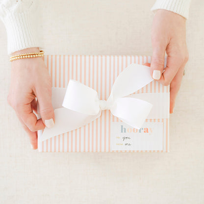 Person tying a bow on top of a pink striped wrapped gift with a hooray birthday sticker