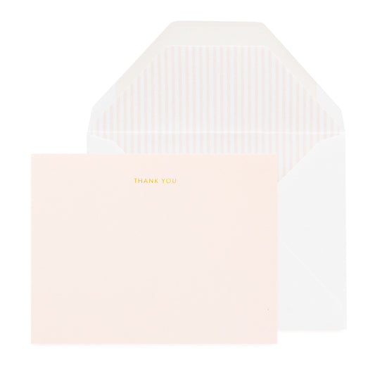 A pale pink thank you note card with 'THANK YOU' printed in gold foil accompanied by a white envelope wiht a striped pink envelope liner